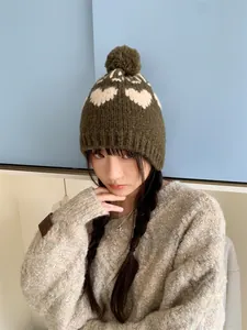 Close-up of a green knit beanie with white heart patterns and a pom-pom on a model