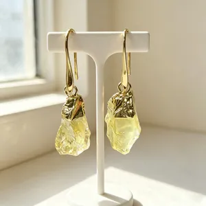 Macro view of raw lemon quartz earrings with gold-plated hooks on a white display stand
