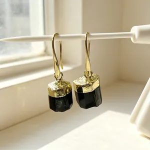 Close-up of gold-plated earrings with natural black tourmaline raw stone pendants.
