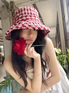 Detail view of a woman wearing a red heart plaid bucket hat holding a red rose