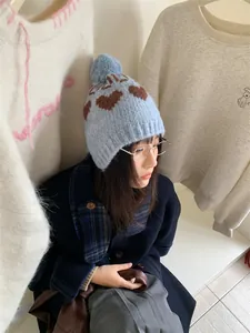 Detailed view of a stylish light blue winter beanie with heart patterns and a soft pom-pom.