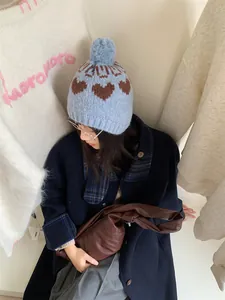 Stylish model wearing a retro light blue heart pattern knit hat with fluffy pom-pom detail
