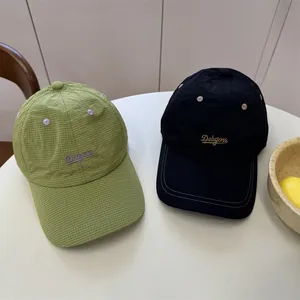 Twee geborduurde baseballpetten in groen ruitpatroon en zwart op een witte tafel.
