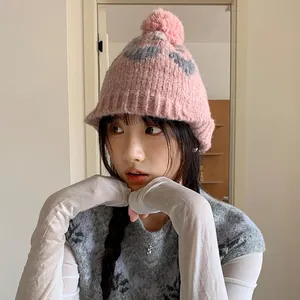 Stylish pink knit beanie featuring grey heart patterns and a plush pom-pom for winter