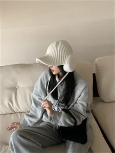 Detailed side view of a white knitted winter hat with earflaps worn by a model