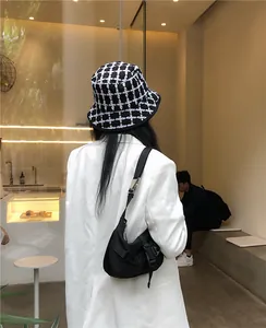 Detail view of a black and white checkered bucket hat worn with a white blazer in a cafe.