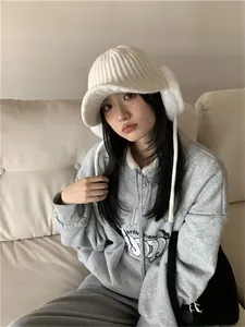 Young woman wearing a warm white knit earflap hat with visor in a cozy indoor setting