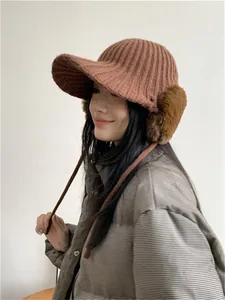 Side profile of woman wearing terracotta knitted winter hat with plush earflaps and brim