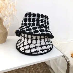 Detailed view of stacked black and white grid knit bucket hats in a minimalist setting.