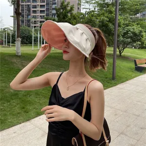 Model trägt einen beige-rosa Sonnenvisierhut mit breiter Krempe in einem Park im Freien.