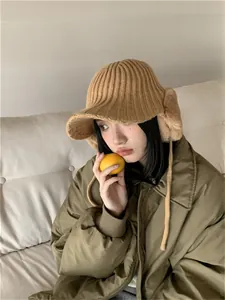 Cozy tan knit trapper hat with plush earflaps worn by model in a stylish winter setting.
