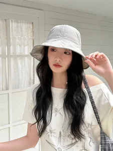 Detail view of a stylish light grey sun protection bucket hat worn by a model outdoors.