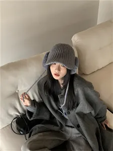Asian model wearing a stylish grey knitted winter hat with ear flaps and brim on a sofa