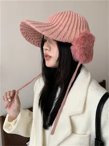 Chic pink knitted winter hat with earflaps and plush pom-poms shown on an Asian model