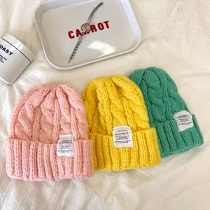 Primo piano di tre berretti in maglia a trecce color caramella rosa, giallo e verde