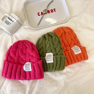 Flatlay di tre berretti in maglia a trecce nei colori fucsia, oliva e arancione