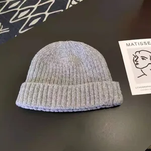 Close-up of a grey ribbed knit beanie hat on a dark surface with an artistic prop card