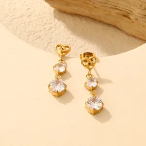 Detaillierte Nahaufnahme eleganter goldener Edelstahl Herz-Zirkonia Ohrringe auf beigem Stativ