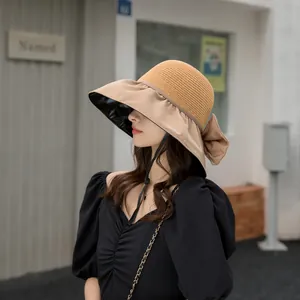 Side view of woman wearing a khaki sun hat with a large brim and a black bow detail