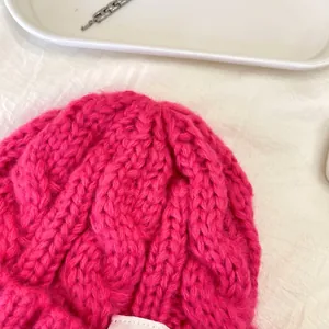 Dettaglio ravvicinato di un berretto in maglia a trecce fucsia con trama di lana calda