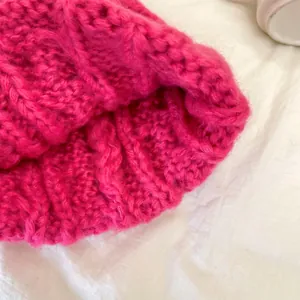 Dettaglio ravvicinato di un berretto in maglia a trecce rosa fucsia in lana