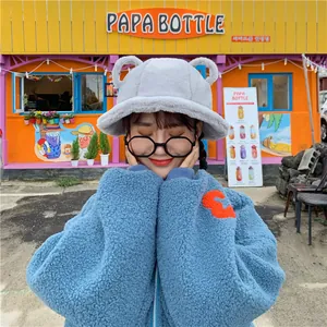 Model wearing a cute grey plush bucket hat with bear ears in a vibrant outdoor setting