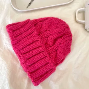 Primo piano del berretto in maglia a trecce rosa magenta con risvolto a coste