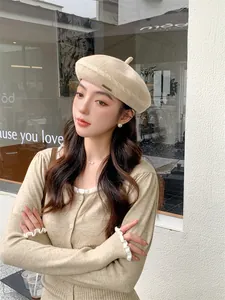 Close-up of a stylish beige knitted beret worn by a model in an outdoor setting.