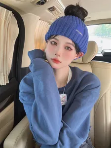 Detail of a blue knitted hairband hat with letter patch worn by a model in a car