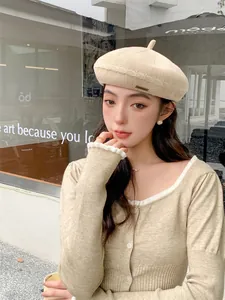 Detail view of a beige knitted beret hat worn by a model in a casual setting