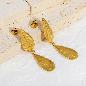 Detail macro view of gold-plated stainless steel leaf drop earrings on textured stone.