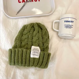 Elegante berretto verde a trecce con toppa vintage per un caldo inverno accogliente.