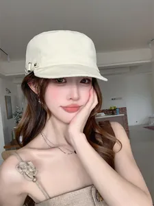 Casquette plate vintage de couleur crème avec détails cloutés portée par une jeune femme