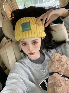 Stylish yellow knitted headband with green letter patch worn by a young woman in a car