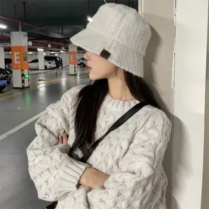 Detailed view of a white plush bucket hat with a small brown patch worn by a model