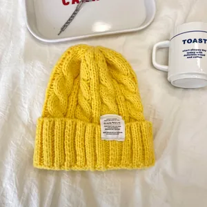 Primo piano di un berretto giallo a maglia a trecce con etichetta decorativa bianca