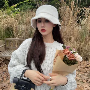 Portrait of a woman wearing a white plush knit bucket hat in an outdoor setting.