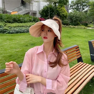 Asiatische Frau im rosa Hemd mit stilvollem beigem Sonnenhut mit breiter Krempe im Park.