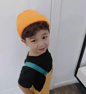 Detailed view of a young Asian boy wearing a vibrant orange knit beanie melon skin hat