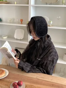 Close-up of a woman wearing black fuzzy lambswool earmuffs in a cozy cafe setting.