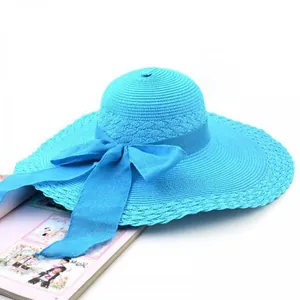 Close-up detail of a bright blue straw sun hat featuring a large ribbon bow and wavy brim
