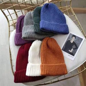 Collection of colorful thick knit beanies in muted tones displayed on a cozy chair