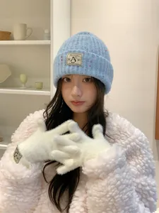 Dettaglio modella con guanti invernali bianchi e berretto blu lavorato a maglia con pinguino