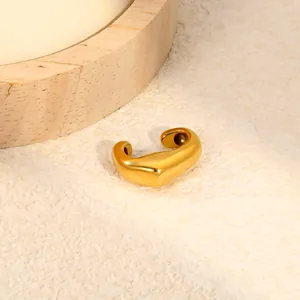 Close-up of a polished gold C-shaped stainless steel ear cuff on a textured background