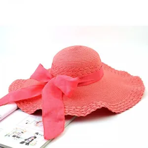 Detailed view of a wide-brimmed pink straw sun hat with a large elegant ribbon bow