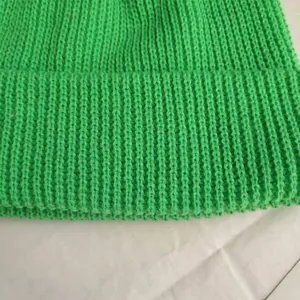 Close-up of bright green short knitted beanie showing ribbed texture and folded edge