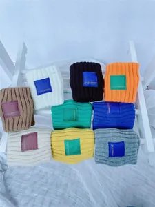 Multiple colors of knitted headbands with letter patches displayed on a stand.