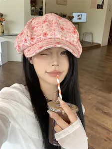 Asian model wearing a stylish pink floral newsboy hat in a cozy cafe background.