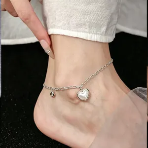 Detail shot of a stainless steel anklet with a white shell heart charm on a foot.