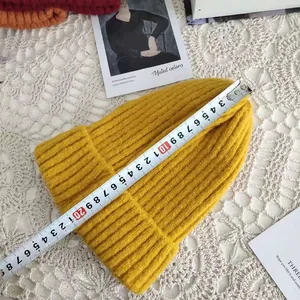 Detail view of a yellow knitted beanie being measured with a tape showing 28cm length